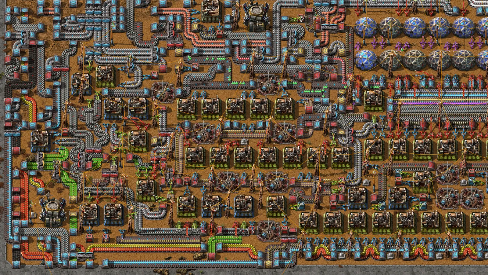 Vista superior de uma fábrica em Factorio, com esteiras transportadoras, máquinas, tubulações e linhas de produção interligadas.