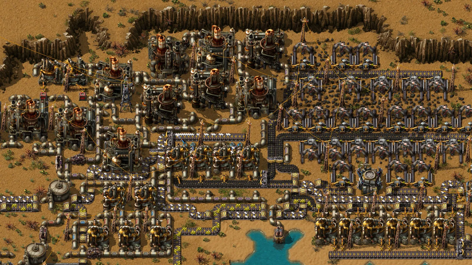 Complexo industrial em Factorio com refinarias, tubulações, esteiras e linhas de produção em terreno desértico.