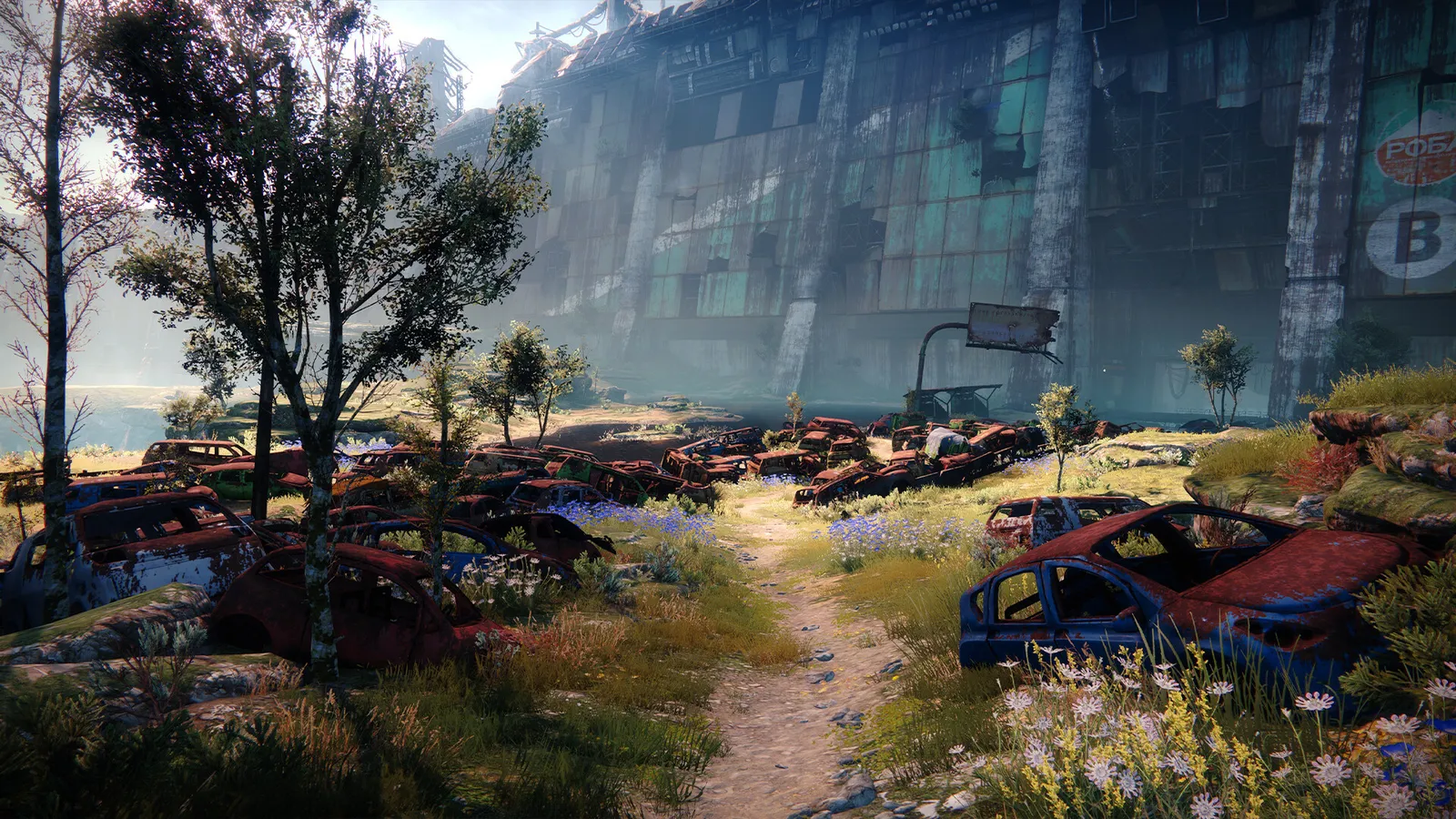 Cena de Destiny 2 mostra carros abandonados em campo florido diante de grande prédio industrial.