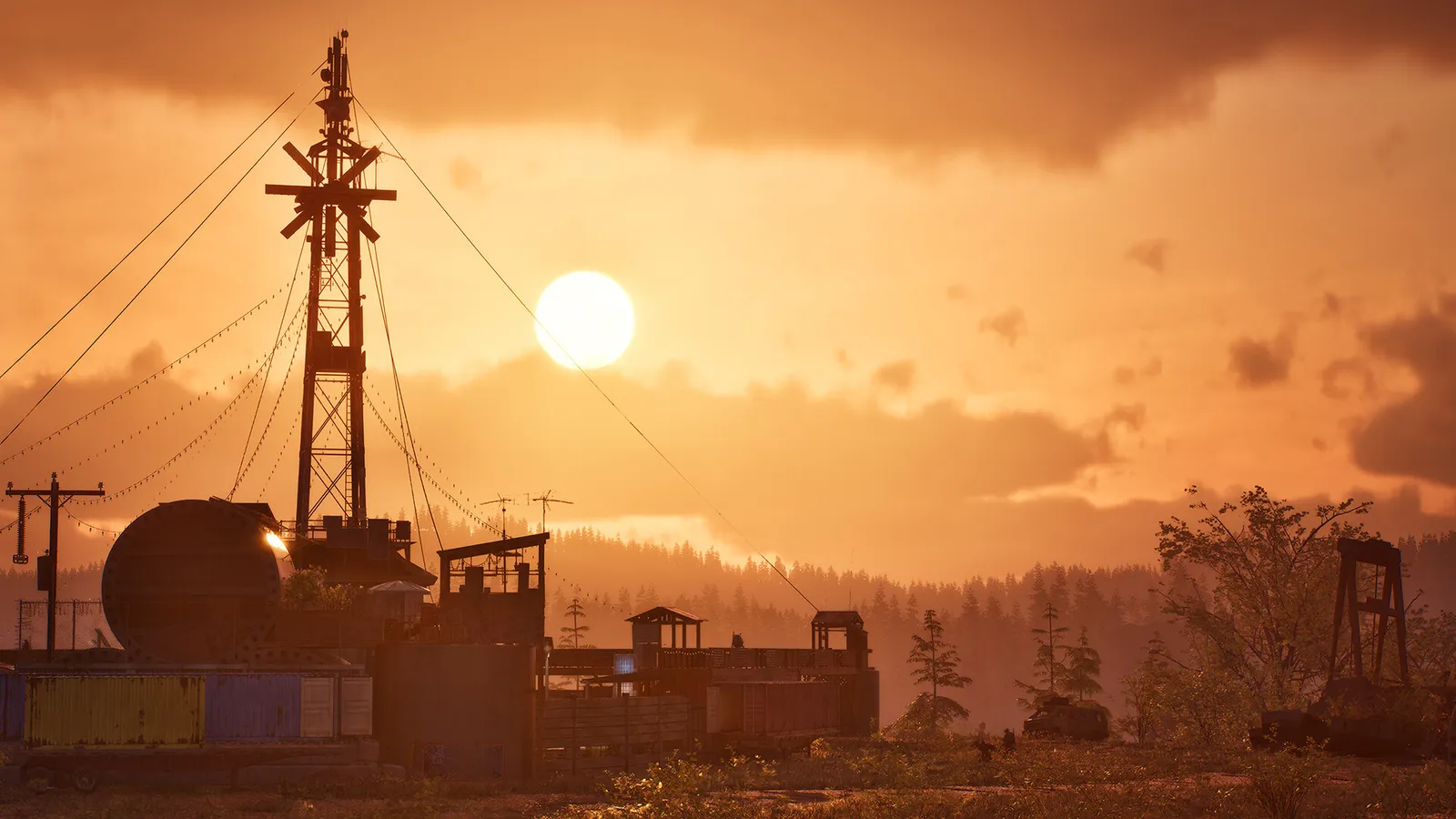 Paisagem industrial ao pôr do sol com torre de comunicação, tanques e construções cercadas por árvores.