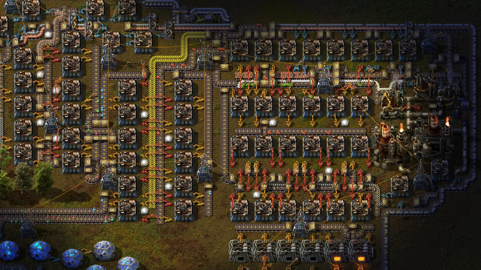 Fábrica em Factorio vista de cima, com esteiras transportadoras, máquinas, tubulações e linhas de produção interligadas.
