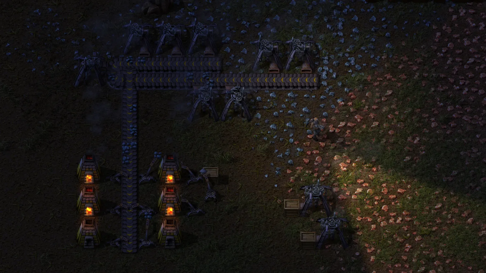 Instalação industrial em Factorio à noite, com mineradoras, esteiras e fornalhas acesas junto a depósitos de minério.