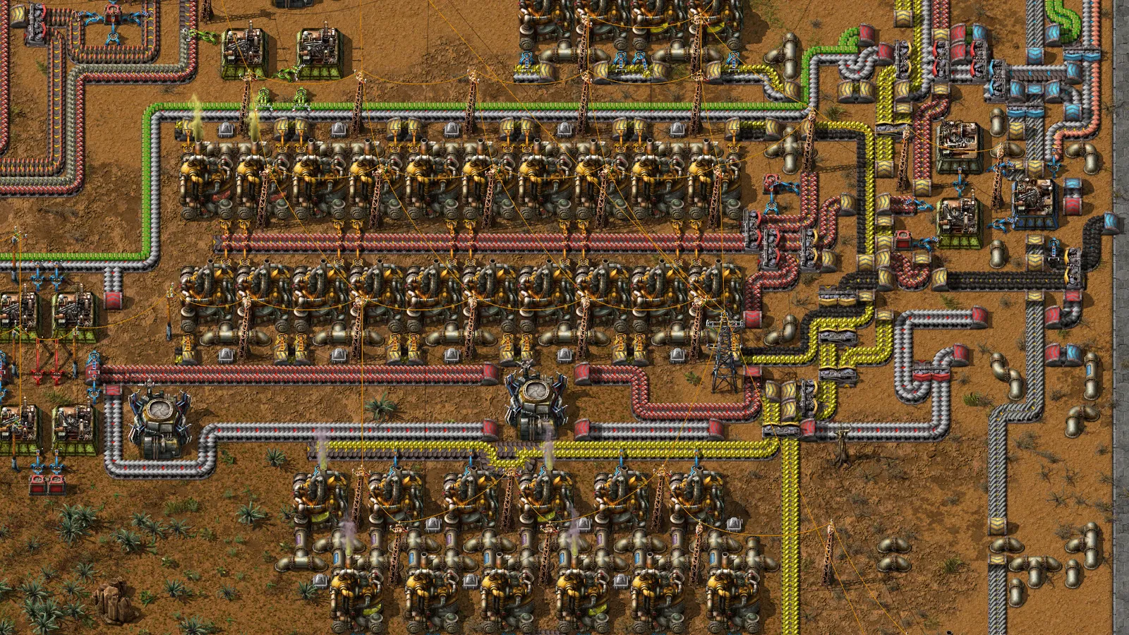 Fábrica em Factorio vista de cima, com fileiras de máquinas, esteiras transportadoras e braços mecânicos sobre terreno árido.