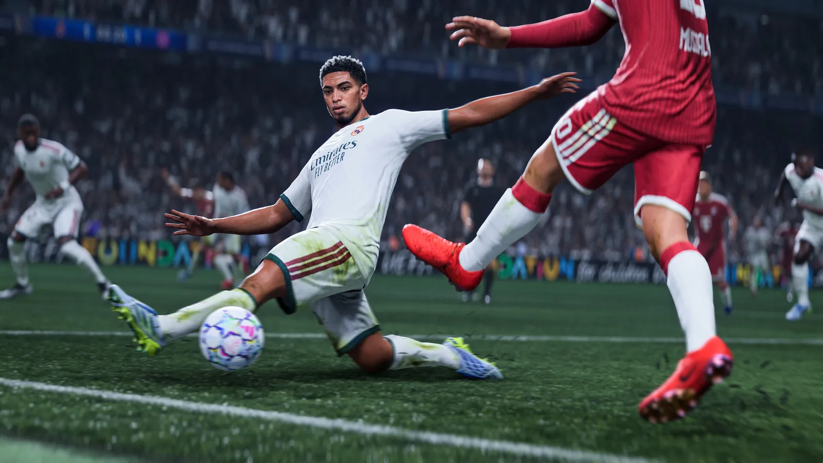 Jogador de uniforme branco desliza para disputar a bola com adversário de uniforme vermelho em estádio de futebol.
