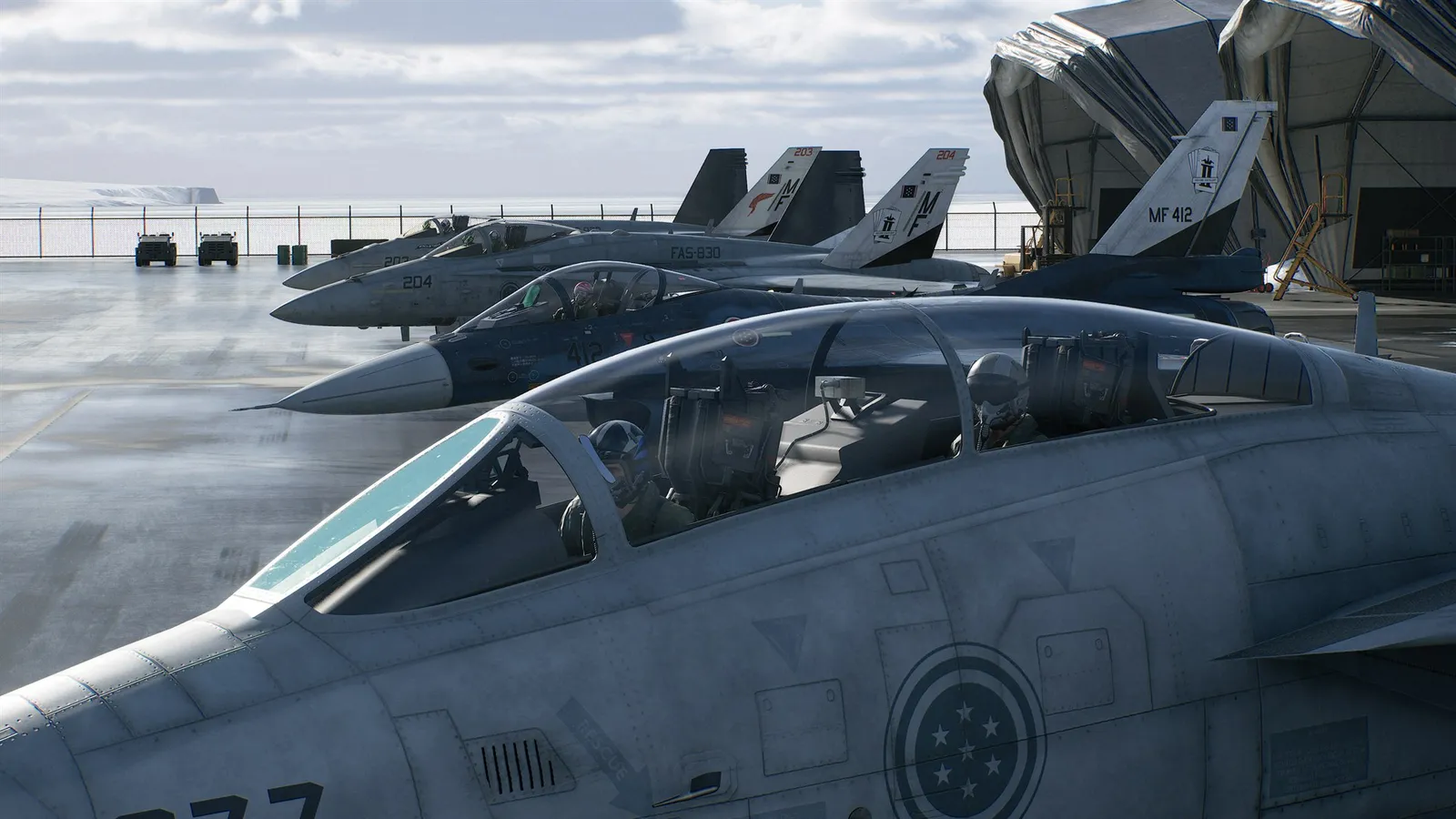 Caças militares estacionados em pista molhada diante de um hangar, vistos da cabine de outro avião.